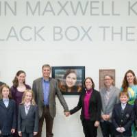 Another photo of the family posing in front of the photo of Linn Maxwell Keller.